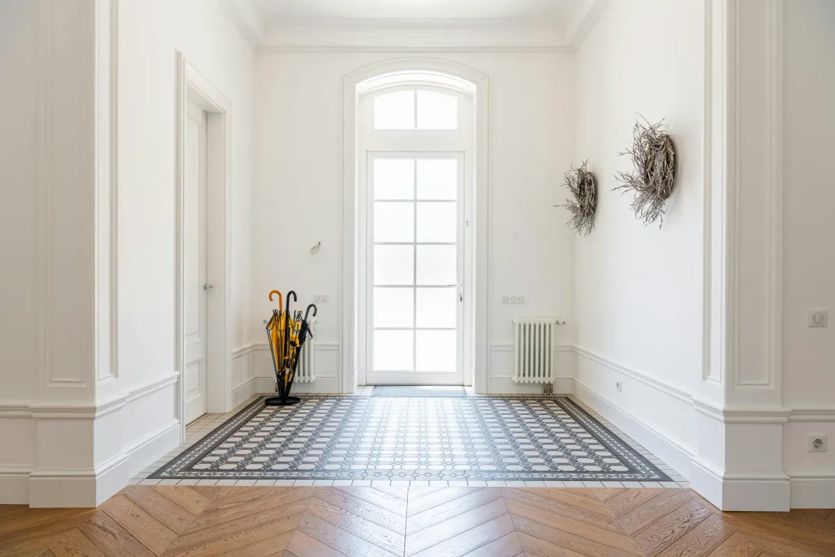 Bright white hallway with herringbone wood floors and a patterned tile inlay