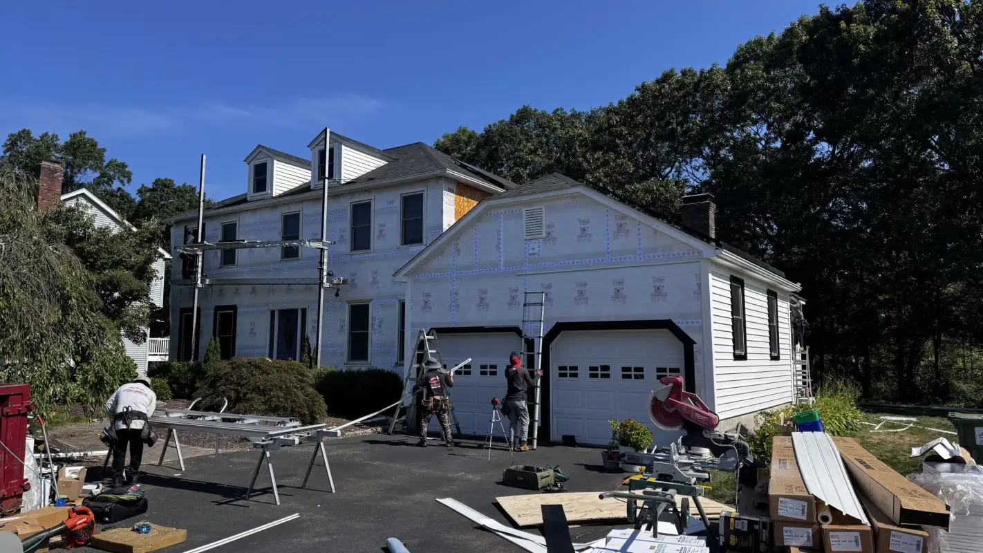 Workers installing white siding on a house with a garage